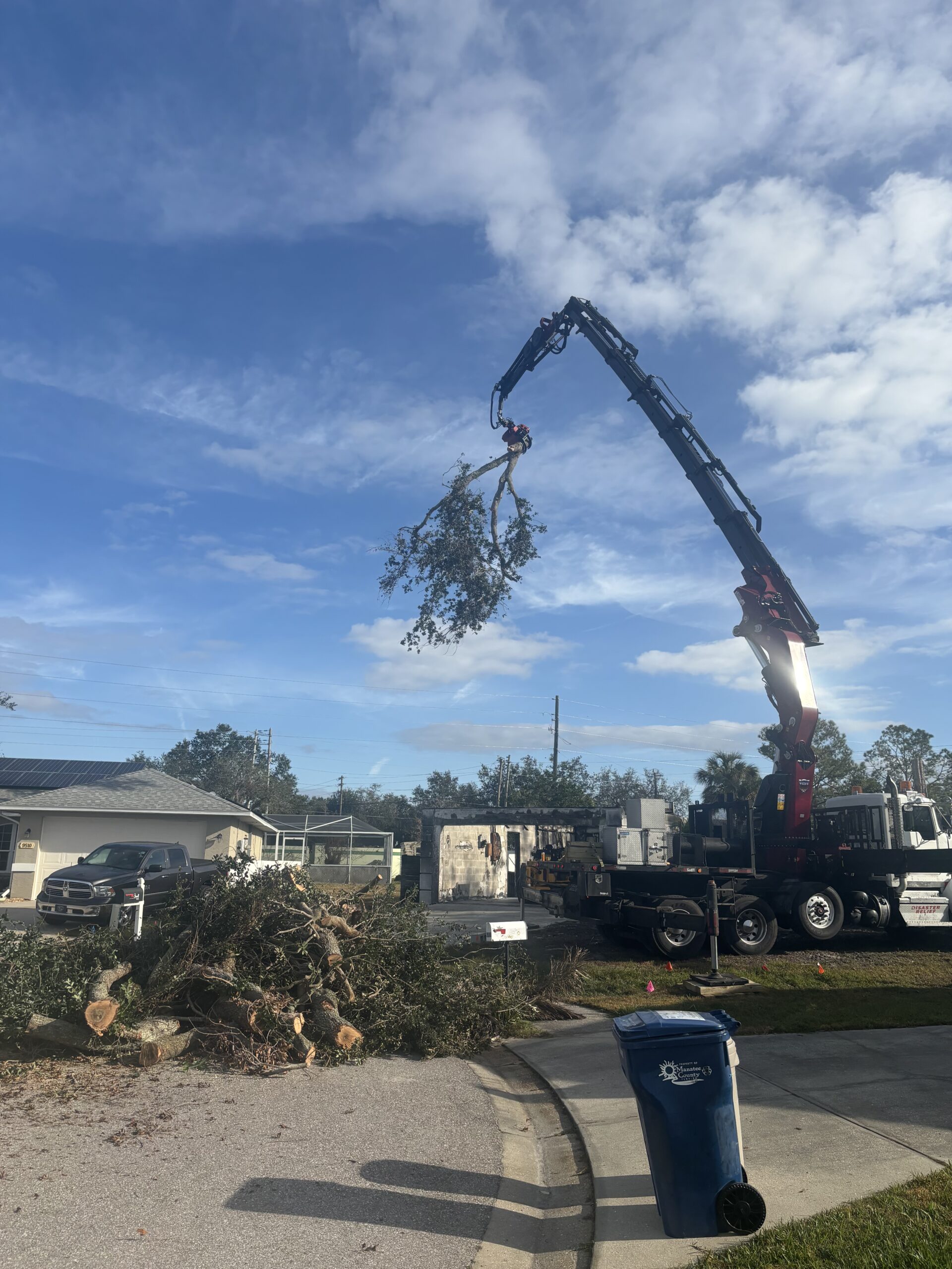 100-ton knuckleboom crane removing trees from a home